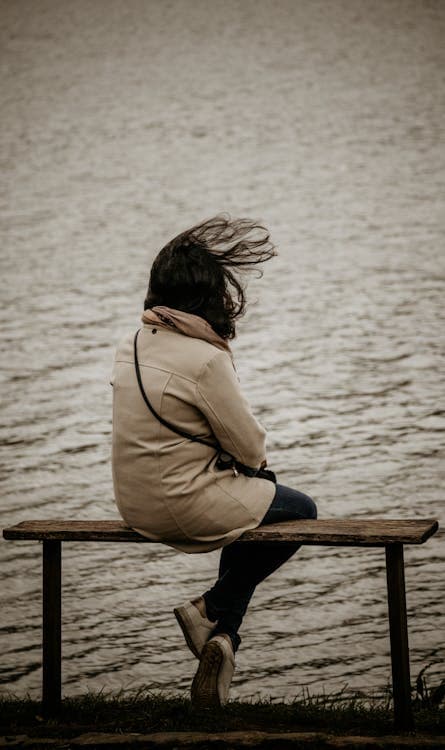 A girl is sitting on a bench near the sea